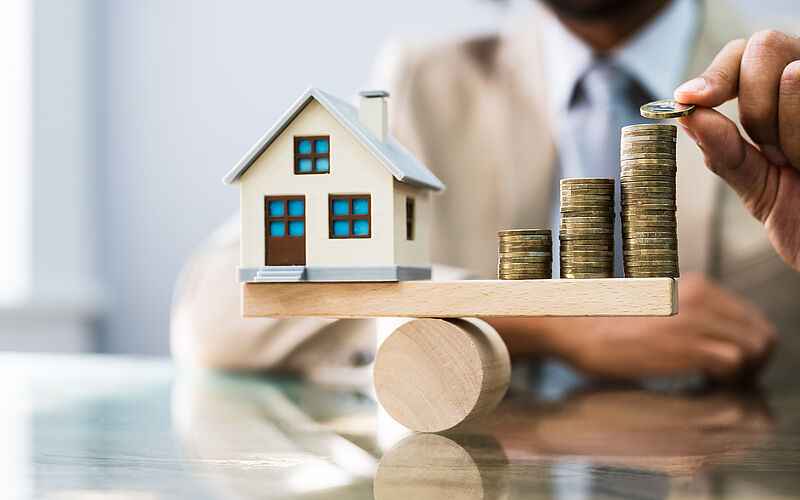 Modellhaus und Geldmünzen auf der Waage 