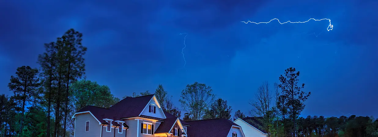 Ein beleuchtetes Einfamilienhaus steht während eines Gewitters unter einem von Blitzen erhellten Himmel.