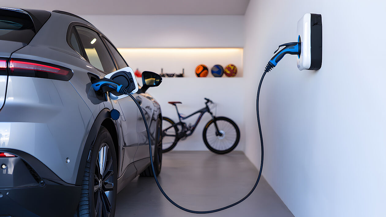Elektroauto lädt gerade, im Hintergrund ist ein Fahrrad und Bälle. 