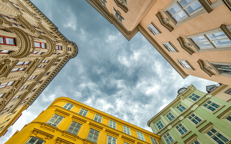 Blick nach oben auf farbige österreichische Altbauwohnungen mit dramatischem Himmel.