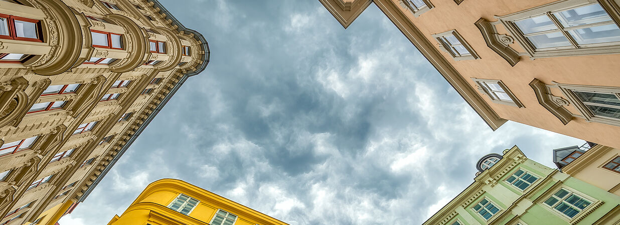 Blick nach oben auf farbige österreichische Altbauwohnungen mit dramatischem Himmel.
