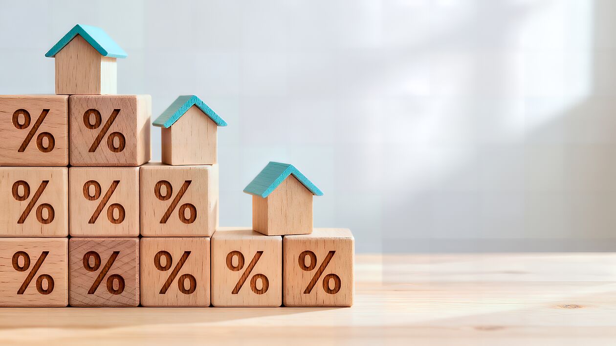 Kleine Holzhäuschen aufReihe Bauklötzchen, die eine Kurve nach unten andeuten.