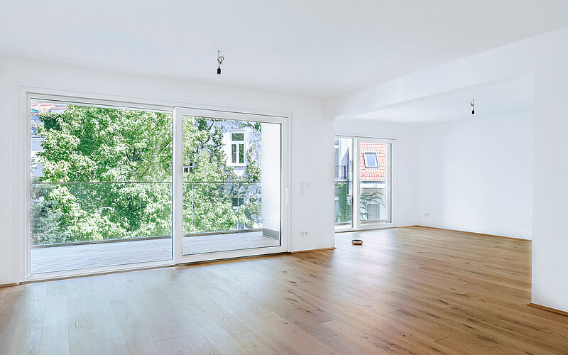 Leerer, moderner Wohnraum mit großen Fenstern und Holzfußboden in einem städtischen Apartment.