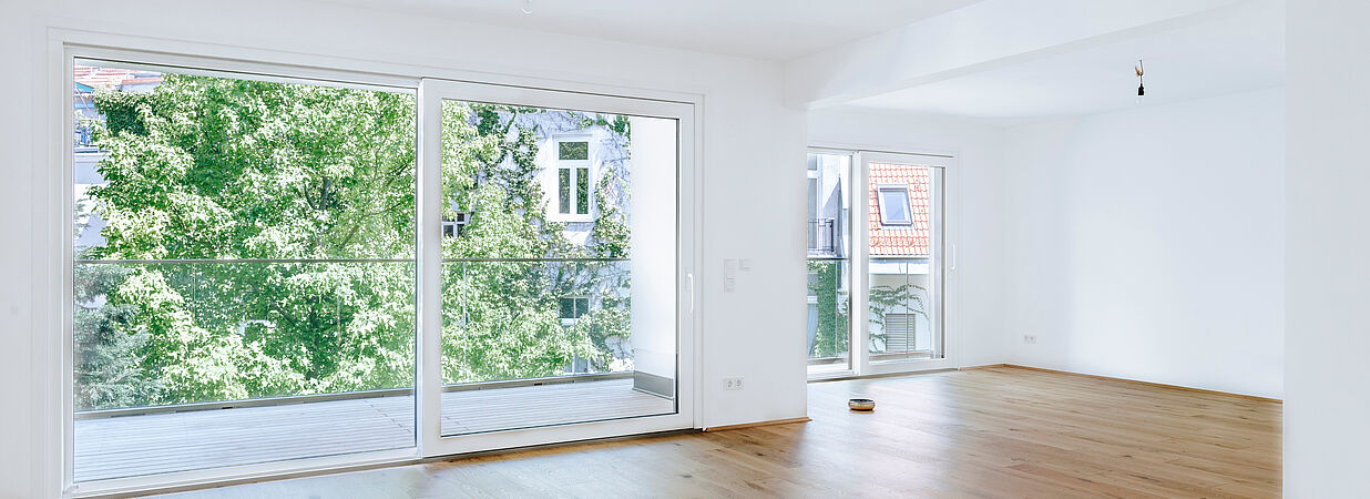 Leerer, moderner Wohnraum mit großen Fenstern und Holzfußboden in einem städtischen Apartment.