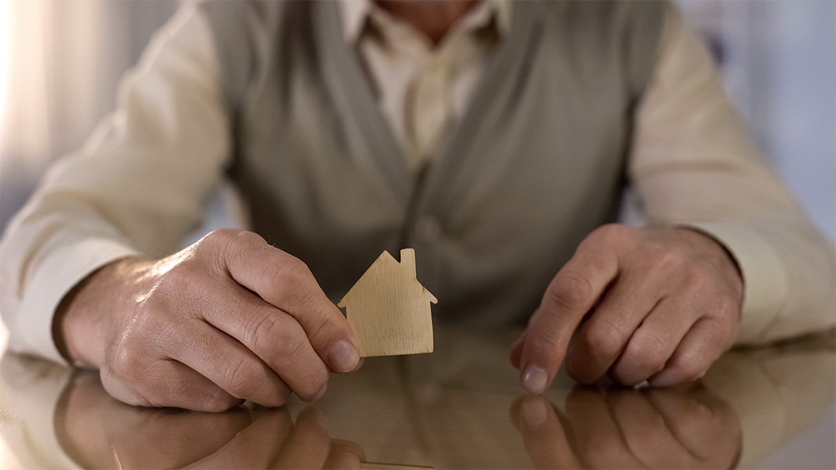 hände eines alten mannes halten ein holzhaus